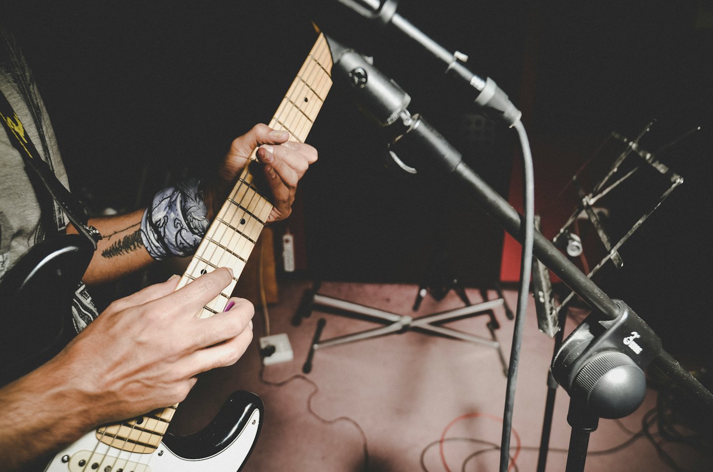 Hände eines Musikers, die eine E-Gitarre mit einem lila Plektrum spielen.